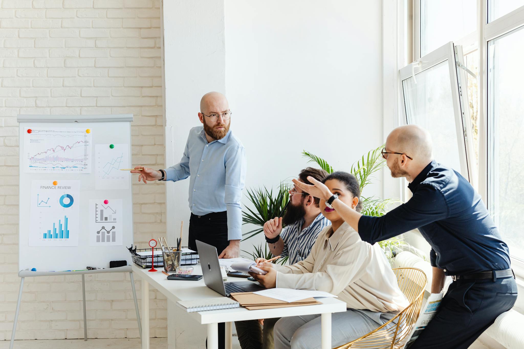 A group of professionals engaged in a business meeting, discussing financial graphs on a whiteboard.